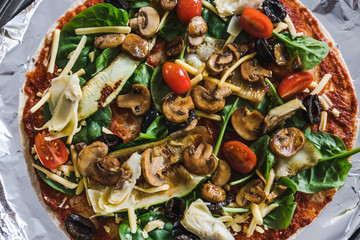 homemade vegan pizza being prepared with tomato spinach chopped veggies and vegan cheese ready to go in the oven