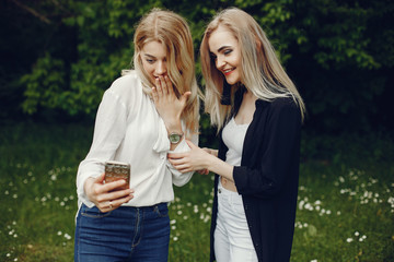 Pretty girls in a summer park. Friends walking in a city. Ladies with blonde hair. Woman use the phone