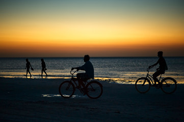 Fototapeta na wymiar Riding bike on Holbox island beach in sunset Mexico. People cycling on the Caribbean beach at sunset.