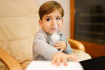 Little small sick boy using steam inhaler nebulizer mask inhalation at home. Medical procedures...