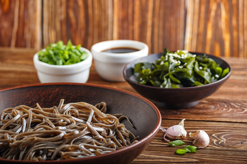Still life of traditional japanese soba noodles with nori (edible seaweed) and soy sauce, on a wooden surface closeup with selective focus