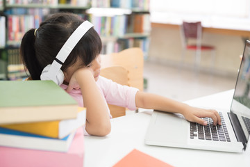 Girls are using computers to study library knowledge. She has earphones at her ear.