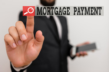 Writing note showing Mortgage Payment. Business concept for periodic amount paid to a holder for repayment of a loan Male human wear formal work suit hold hi tech smartphone use hand