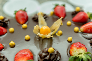 Closeup of chocolate cake with physalis and strawberry. Delicious birthday party dessert. Chocolate and fruits. Festive and celebration concept. Selective focus.