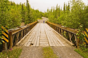 Fototapeta premium Person walking along an old steel construction bridge in Yukon, Canada