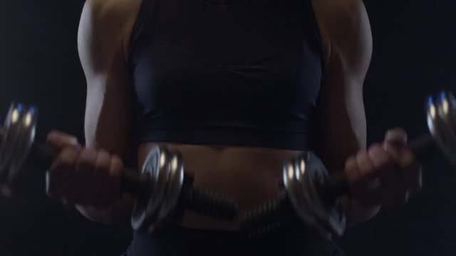 Fit woman doing biceps curls with dumbbells, close up, shot in slow motion