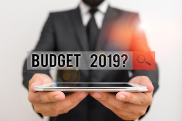 Text sign showing Budget 2019 Question. Business photo text estimate of income and expenditure for next year Male human wear formal work suit hold smart hi tech smartphone use hands