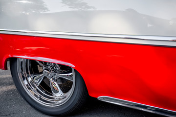 Rear wheel with chrome rim under a low quarter of a red and white vintage retro car