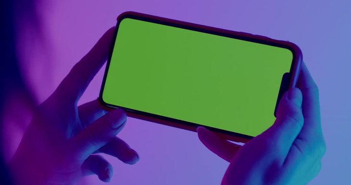 GREEN SCREEN CHROMA KEY CU Caucasian female holding modern smart phone, horizontal orientation, colorful neon background. 4K UHD RAW Graded footage