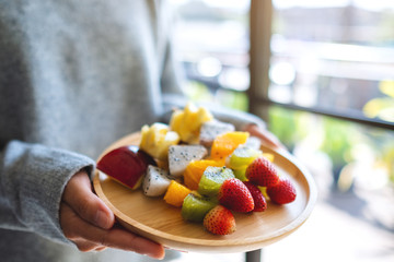 Closeup image of a woman holding a wooden plate of fresh mixed fruits on skewers