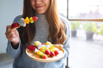 Closeup image of an asian woman holding and eating a fresh mixed fruits on skewers