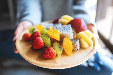 Closeup image of a woman holding a wooden plate of fresh mixed fruits on skewers