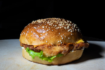 Burger with chicken and green salad on a cutting board, on a black background.