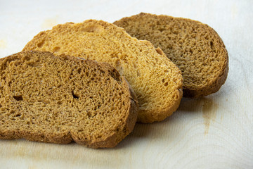 Two slices of dark bread and one white bread lie on a wooden cutting board.