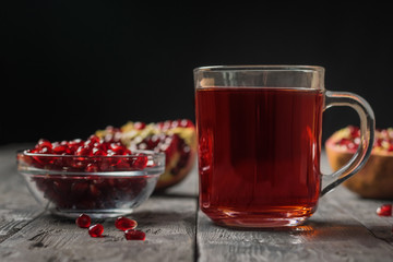 Fresh pomegranate fruit and pomegranate juice in a glass mug on a wooden table.