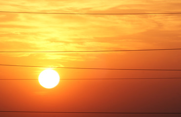 Yellow sun at dawn and line of wires.