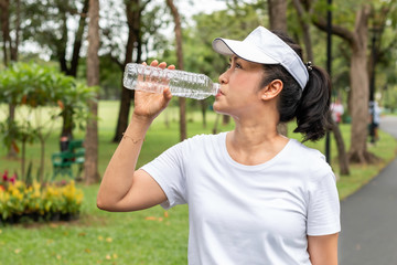 Relaxing time.Asian smiling senior woman drinking fresh water in summer at the park.