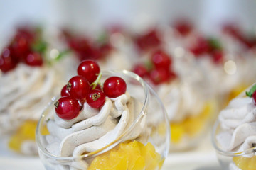 Mini cakes decorated with whipped cream and fresh red currant. Sweet tasty snacks at the party. Food photography. Lots of pastry pieces on the plate