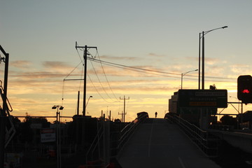 Lone bicycle cyclist riding across a city bridge on a summer day after work riding into the sunset, Melbourne city, Victoria, Australia, 6 July 2019