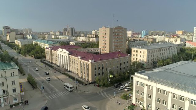 Aerial above Yakutsk cityscape city center capital of Sakha Republic. Far East. City permafrost. Old new soviet buildings city ​​life Siberia. Road traffic cars ride a crossroads. Sunny day blue sky