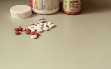 Variety of pill medicines and vitamins mixed loosely with bottles in the background