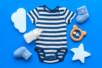 Blue bodysuit for baby boy near children's accessories on blue background top-down