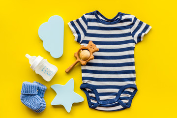 Blue bodysuit for baby boy near children's accessories on yellow background top-down