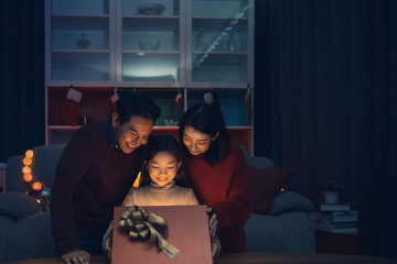 Happy family and little girl open magic gift box with light shining in living room that decorated with Christmas tree for Christmas festival coming soon, Asian Christmas family concept