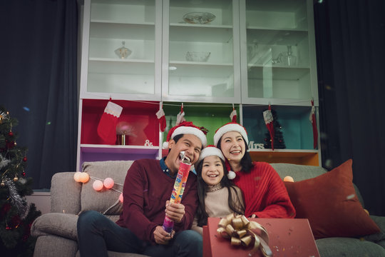 happy family man, woman, little girl play firecracker, firework to celebrate "New Year" together at christmas day night in room that decorated with christmas tree for Asian christmas festival day