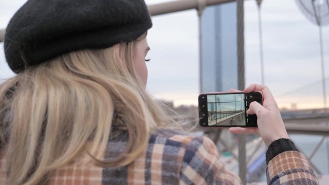 Tourist woman taking photos on her mobile device of NYC from Brooklyn Bridge