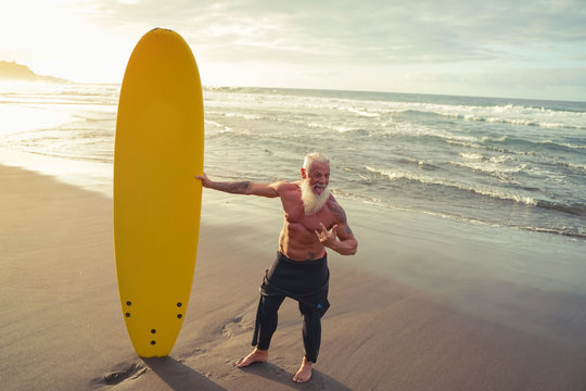 Fit senior having fun surfing at sunset time - Sporty bearded man training with surfboard on the beach - Elderly healthy people lifestyle and extreme sport concept - Image
