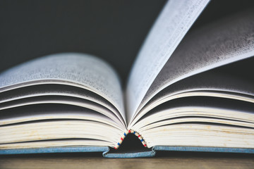 An old book open on wooden table with black color wall background copy space