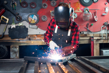 Beautiful young woman welder engineer stands in apron on background of tools crafting. Concept...