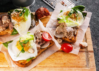 Sea food sandwich. Cod liver, fresh lettuce, pea sprouts, tomatoes and fried eggs. Healty and tasty breakfast on a cutting wooden board.
