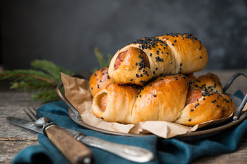 Sausages baked in dough and sprinkled with black sesame on a gray background.