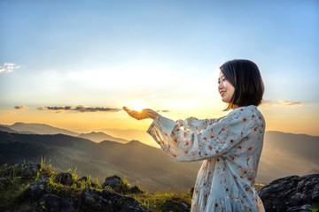 Happiness Asian beauty woman in flower dress with hand holding a sunshine on beautiful scenic view with mountain and sunlight background.Relaxing freedom in nature.Holiday Vacation Travel.