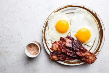 Fried eggs and bacon for breakfast on a plate, top view, copyspace