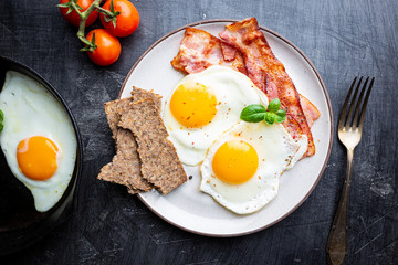 Fried eggs and bacon for breakfast on a plate, top view, copyspace