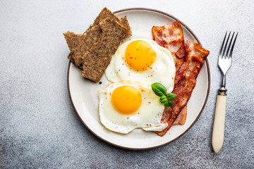 Fried eggs and bacon for breakfast on a plate, top view, copyspace