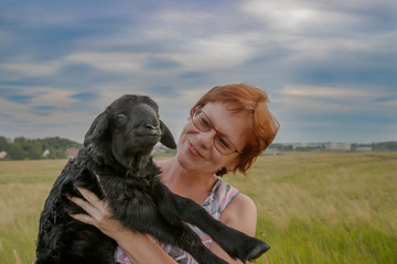Woman holds little lamb in the field