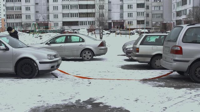 A man gets into broken car to be towed by another automobile using a flexible rope hawser hitch. Winter daytime in parking lot of yard. Malfunction or problem with auto. Bad and cold weather