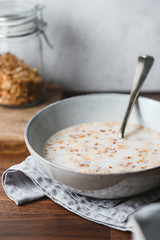 Baked granola and almond milk in a ceramic bowl on breakfast table.