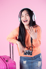 Asian tourist woman wearing sweater using headphone and luggage  on pink background, travel concept.