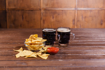 Two mugs of beer with snacks on wooden table