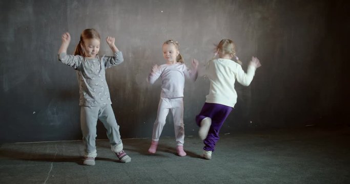 Three little five year old girlfriends having fun frolic and leaping in the room.
