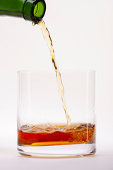 Close-up of an elegant glass for spirits, with a spilled liquor, similar to rum or whiskey, on a white background.