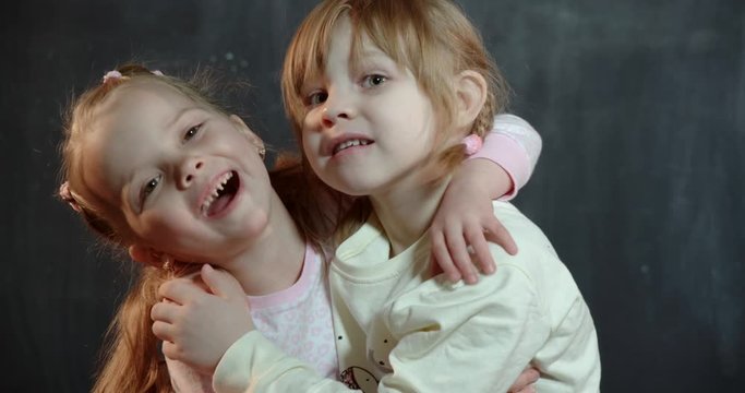 Two cute babies of five years of age laugh and friendly hugging while looking at the camera.
