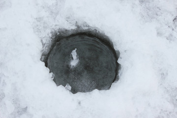 Wormwood, Ice hole in frozen water. A frozen hole drilled in ice with a drill. View from above. A frozen hole in a river. Winter fishing - Powered by Adobe