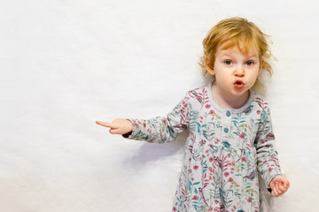 Girl, three years old, looking at the camera and pointing a finger to the side. Copy space.