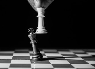 Black and white image of white king taking down black king. Hand and fingers and chess board